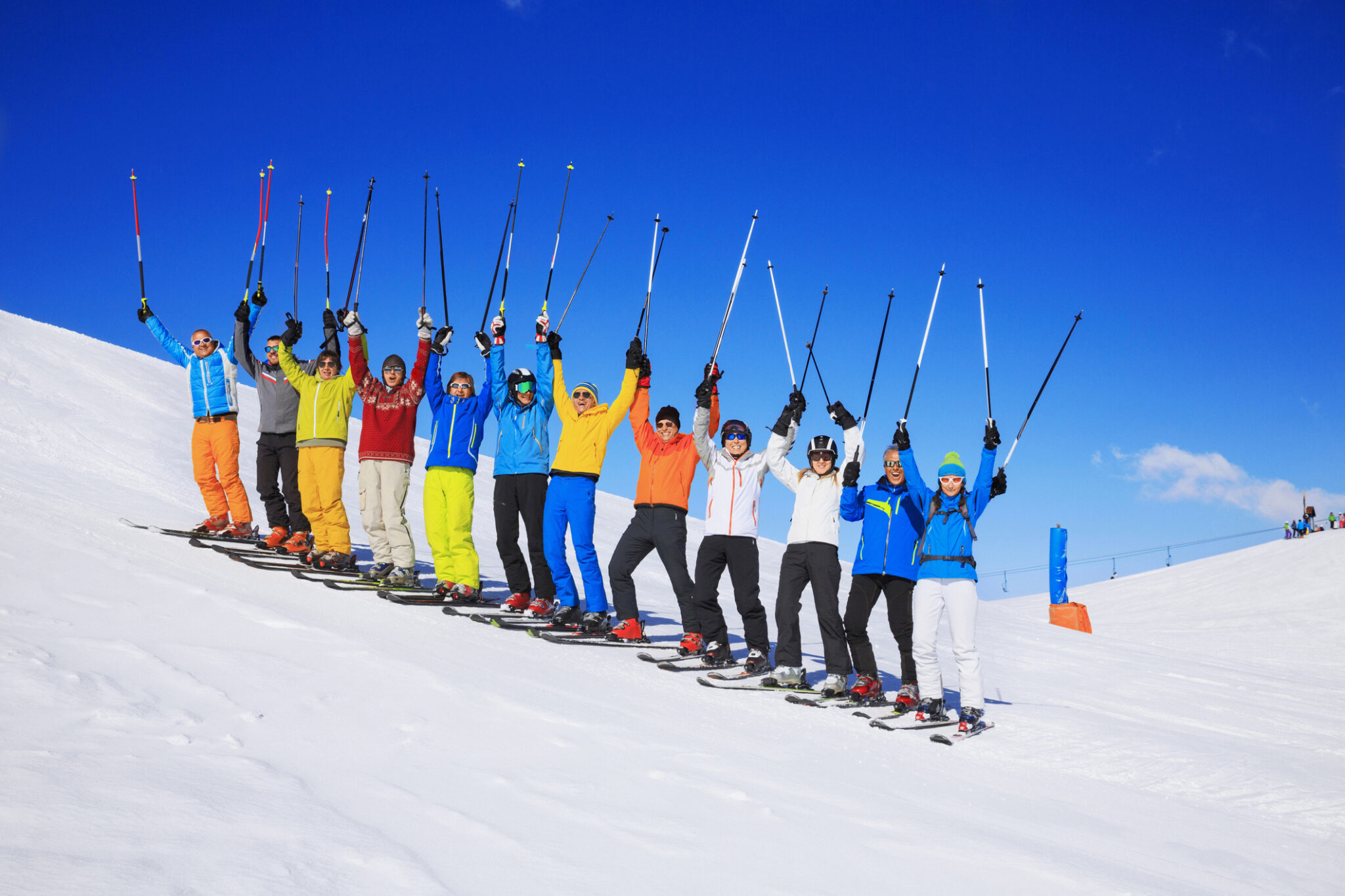A large happy group of snow skiers. Ski club school skiing trips. Friends - Colorful male and female groups, enjoying on sunny ski resorts.  The snow in the foreground, beautiful blue sky in the background, applicable for all ski resorts and locations.  Shot with Canon 5DMarkIII, developed from RAW, Adobe RGB color profile.